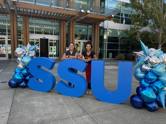 An image of SSU's repatration staff standing behind a blue SSU sign with decorative balloons